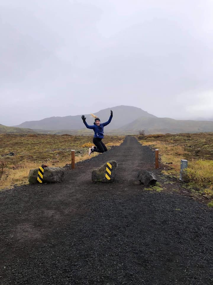 A person jumps with joy in front of a road leading into the wilderness